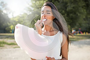 Beautiful brunette woman with cotton candy and windy hair, with backpack walking in the park and looking at the camera