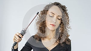 Beautiful brunette woman with curly hair, curls her hair, uses curling tongs to get fine curls. A girl makes her own