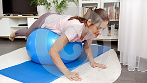 Beautiful brunette woman doing fitness exercises while rolling on big blue fit ball at home