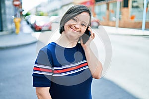 Beautiful brunette woman with down syndrome at the town on a sunny day talking on smartphone