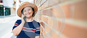 Beautiful brunette woman with down syndrome at the town on a sunny day talking on smartphone leaning on a bricks wall