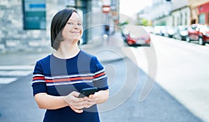 Beautiful brunette woman with down syndrome at the town on a sunny day using smartphone