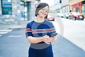 Beautiful brunette woman with down syndrome at the town on a sunny day using smartphone