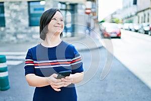 Beautiful brunette woman with down syndrome at the town on a sunny day using smartphone