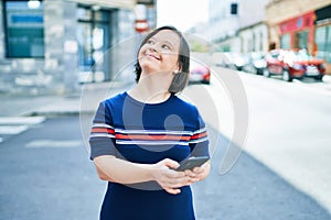 Beautiful brunette woman with down syndrome at the town on a sunny day using smartphone