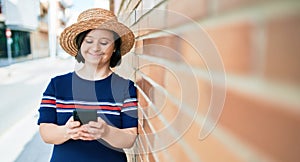 Beautiful brunette woman with down syndrome at the town on a sunny day using smartphone leaning on a bricks wall