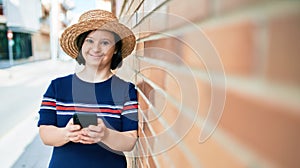 Beautiful brunette woman with down syndrome at the town on a sunny day using smartphone leaning on a bricks wall