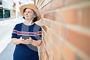 Beautiful brunette woman with down syndrome at the town on a sunny day using smartphone leaning on a bricks wall