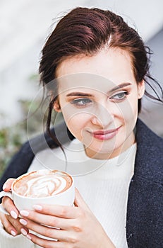 Beautiful brunette woman drinking cappuccino coffee with foam inthe street cafe