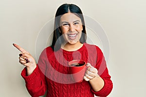 Beautiful brunette woman drinking a cup of black coffee smiling happy pointing with hand and finger to the side