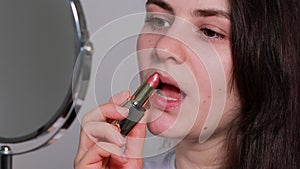 Beautiful brunette woman dyes her lips with lipstick in front of the mirror. Natural simple make-up at home on your own.