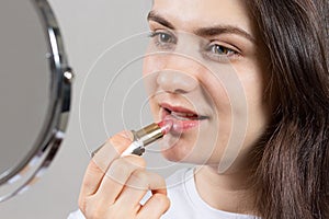 Beautiful brunette woman dyes her lips with lipstick in front of the mirror. Natural simple make-up at home on your own.