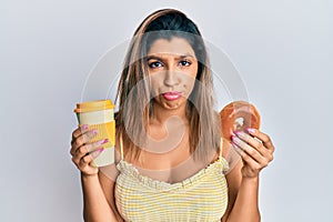 Beautiful brunette woman eating doughnut and drinking coffee depressed and worry for distress, crying angry and afraid