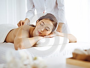 Beautiful brunette woman enjoying back massage with closed eyes. Spa and medicine concept