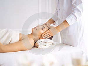 Beautiful brunette woman enjoying facial massage with closed eyes. Relaxing treatment in medicine and spa center