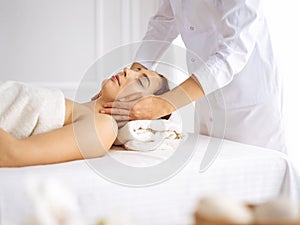 Beautiful brunette woman enjoying facial massage with closed eyes. Relaxing treatment in medicine and spa center