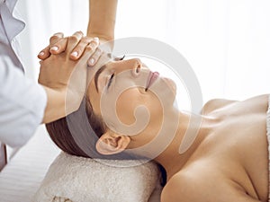 Beautiful brunette woman enjoying facial massage with closed eyes. Relaxing treatment in medicine and spa center