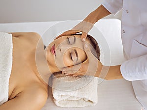 Beautiful brunette woman enjoying facial massage with closed eyes. Relaxing treatment in medicine and spa center