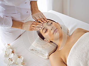 Beautiful brunette woman enjoying facial massage with closed eyes. Relaxing treatment in medicine and spa center