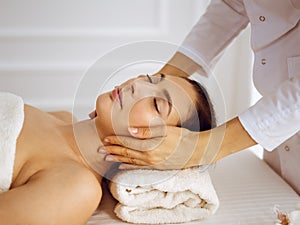 Beautiful brunette woman enjoying facial massage with closed eyes. Relaxing treatment in medicine and spa center