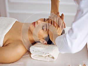 Beautiful brunette woman enjoying facial massage with closed eyes. Relaxing treatment in medicine and spa center