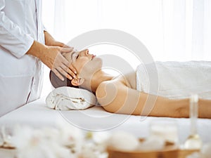 Beautiful brunette woman enjoying facial massage with closed eyes. Relaxing treatment in medicine and spa center