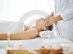 Beautiful brunette woman enjoying facial massage with closed eyes. Relaxing treatment in medicine and spa center