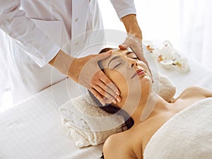 Beautiful brunette woman enjoying facial massage with closed eyes. Relaxing treatment in medicine and spa center