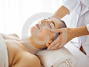 Beautiful brunette woman enjoying facial massage with closed eyes. Relaxing treatment in medicine and spa center