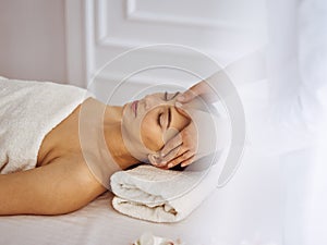 Beautiful brunette woman enjoying facial massage with closed eyes. Relaxing treatment in medicine and spa center