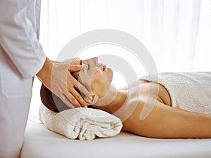 Beautiful brunette woman enjoying facial massage with closed eyes. Relaxing treatment in medicine and spa center