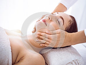 Beautiful brunette woman enjoying facial massage with closed eyes in sunny spa center . Relaxing treatment and cosmetic