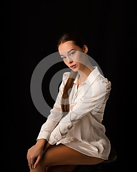 Beautiful brunette woman girl sexy model, dressed in a white silk shirt on the body. Graceful hip and knee. Looks into the frame