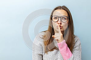 Beautiful brunette woman in glasses holding finger on lips and showing silence sign, asking to keep silent about her secret