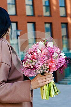 Beautiful brunette woman holding bridal bouquet in pink lilac tones made of hyacinth, tulips and gypsophila