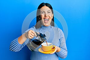Beautiful brunette woman holding french coffee maker pouring coffee on cup smiling and laughing hard out loud because funny crazy