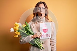 Beautiful brunette woman holding love mom message and tulips celebrating mothers day scared in shock with a surprise face, afraid