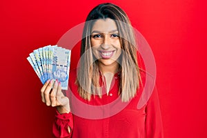 Beautiful brunette woman holding south african 100 rand banknotes looking positive and happy standing and smiling with a confident