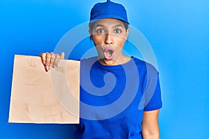 Beautiful brunette woman holding take away paper bag scared and amazed with open mouth for surprise, disbelief face