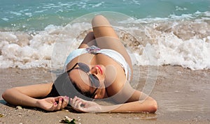 Beautiful brunette woman lies on the beach in waves