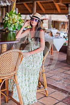 Beautiful brunette woman in long dress and hat relaxing in beach restaraunt