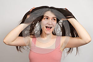 A beautiful brunette woman with long hair on a white background holds her hands on her head and thinks about what