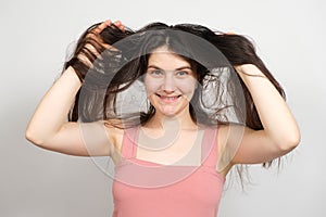 A beautiful brunette woman with long hair on a white background holds her hands on her head and thinks about what