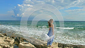Beautiful brunette woman in maxi dress enjoying windy day on seashore, vacation