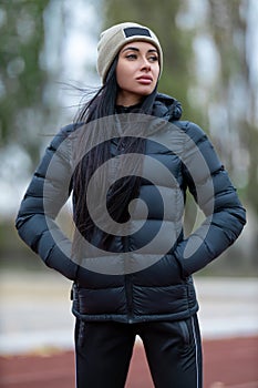 Beautiful brunette woman posing at the sport stadium in jacket and hat