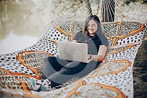 Beautiful brunette woman relaxing on hammock outdoors near lake in the forest, freelancer working in the park while resting in
