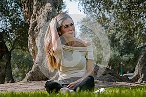 Beautiful brunette woman touching her long hair. She sits in a park on green grass.