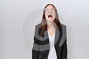 Beautiful brunette woman wearing business jacket and glasses angry and mad screaming frustrated and furious, shouting with anger