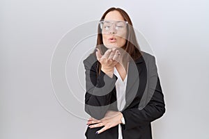 Beautiful brunette woman wearing business jacket and glasses looking at the camera blowing a kiss with hand on air being lovely