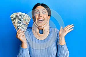 Beautiful brunette woman wearing cervical collar holding insurance money celebrating achievement with happy smile and winner